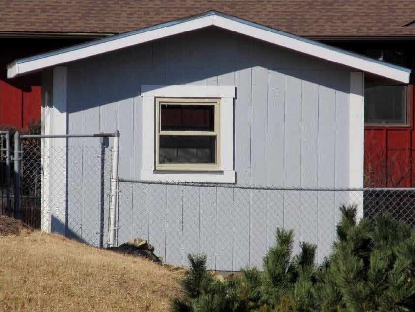gray tool shed with white trim and a window surrounded by a chain-link fence